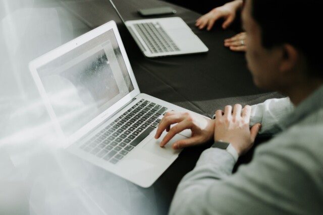 Zwei Personen arbeiten an ihren Laptops nebeneinander an einem Tisch
